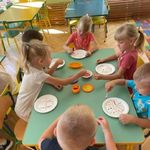 Dzieci siedzą przy stolikach i ozdabiają papierowe talerzyki kolorowymi  kropkami z farby