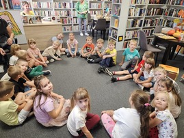 Dzieci siedzą w kole na dywanie w bibliotece.jpg