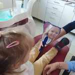dziewczynka siedzi na fotelu stomatologicznym i przegląda swoje zęby w lusterku