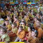 Przedszkolaki w sali siedzą na dywanie