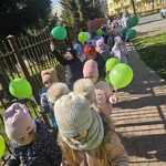 Dzieci idą na spacer niosąc zielone balony  - symbol wiosny.