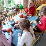 Dzieci siedzą przy stoliku, oglądają warzywa przez lupy.