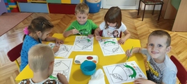 Dzieci siedzą przy stoliku i malują farbami grzybki.jpg