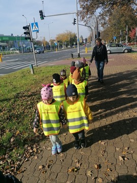 Dzieci ubrane w kamizelki odblaskowe idą na spacer na skrzyżowanie ulic.