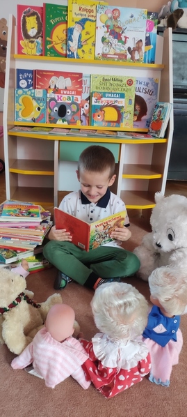 Chłopiec czyta książeczkę misiom i lalkom.jpg