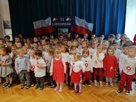 Przedszkolaki stoją i śpiewają piosenki patriotyczne oraz hymn Polski.